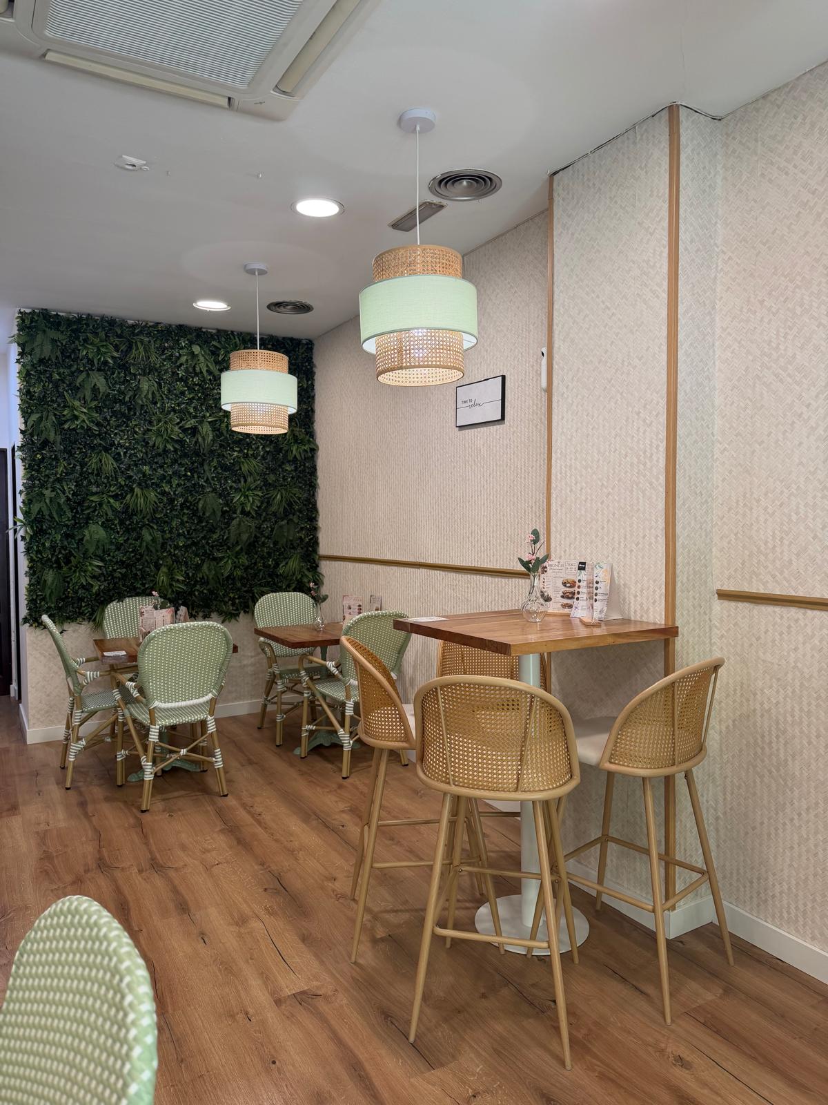 Sala con jardín vertical, sillas de ratán verde menta y mesas altas en Mediterránea Café Actur Zaragoza