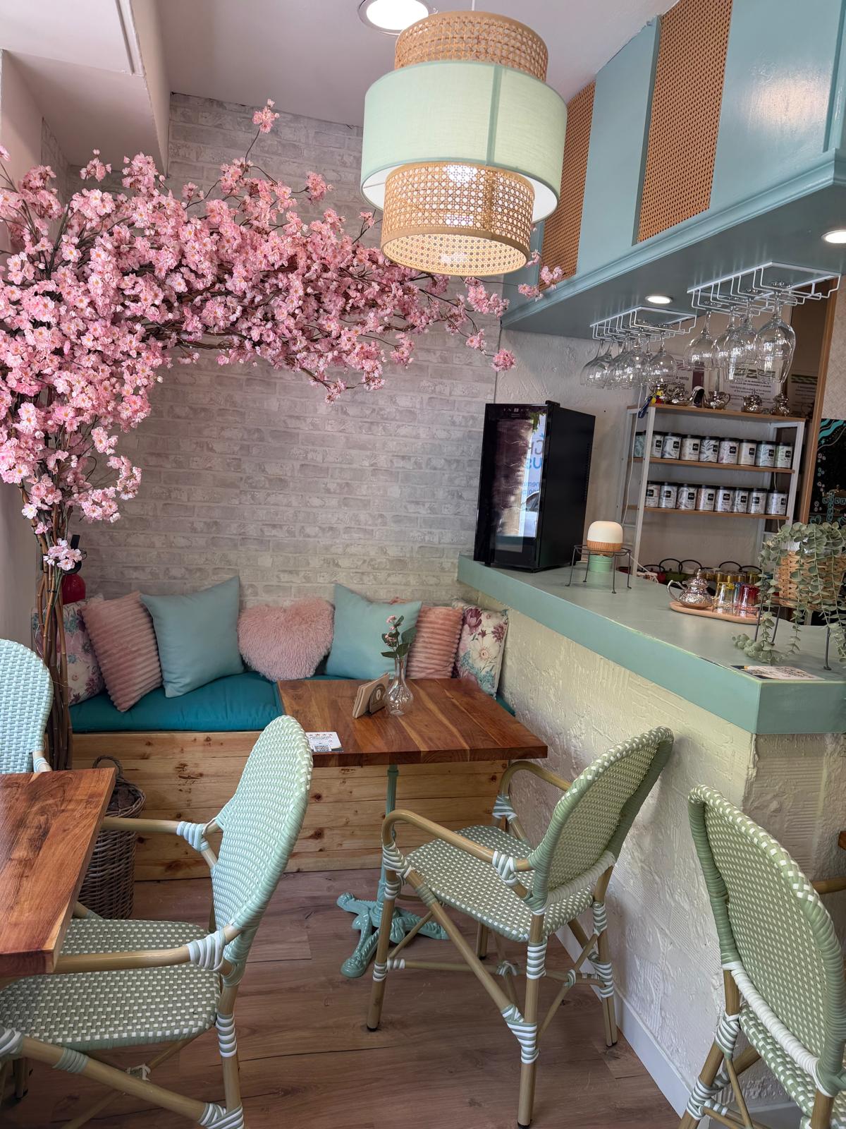 Sala de Mediterránea Café con cerezo en flor, sofá de cojines turquesa y barra verde menta en Zaragoza